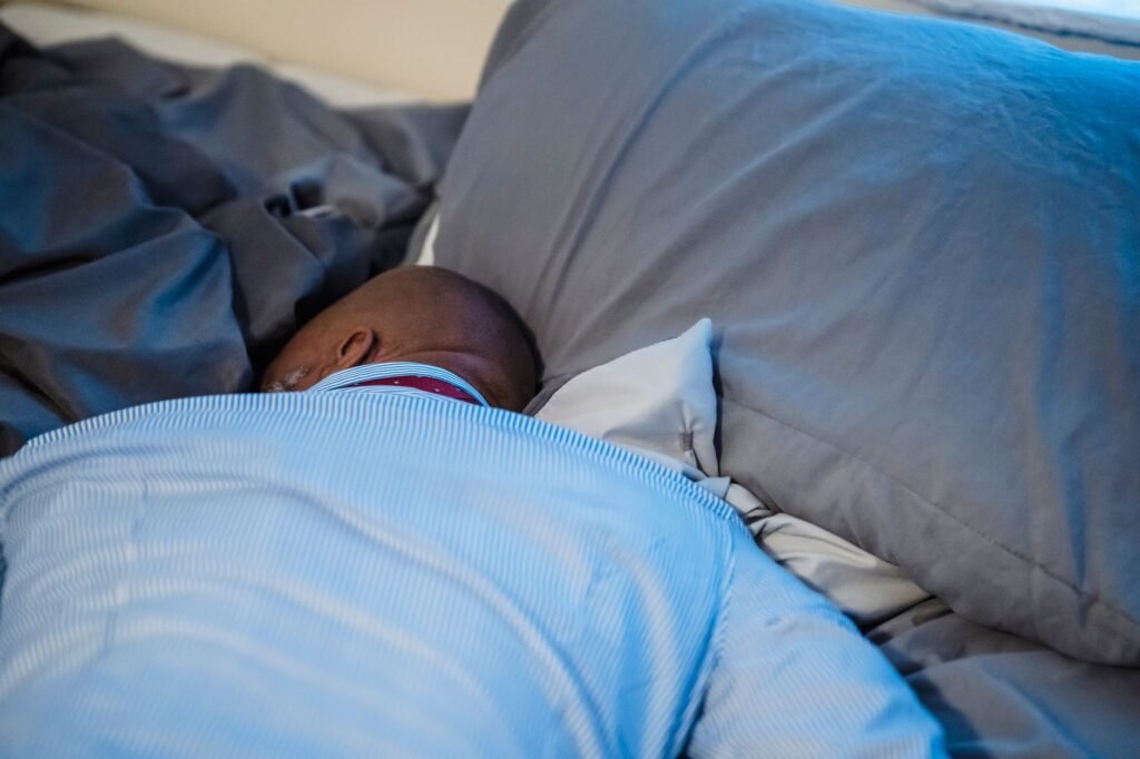 An adult resting peacefully on a bed with soft gray bedding, captured in an indoor setting.