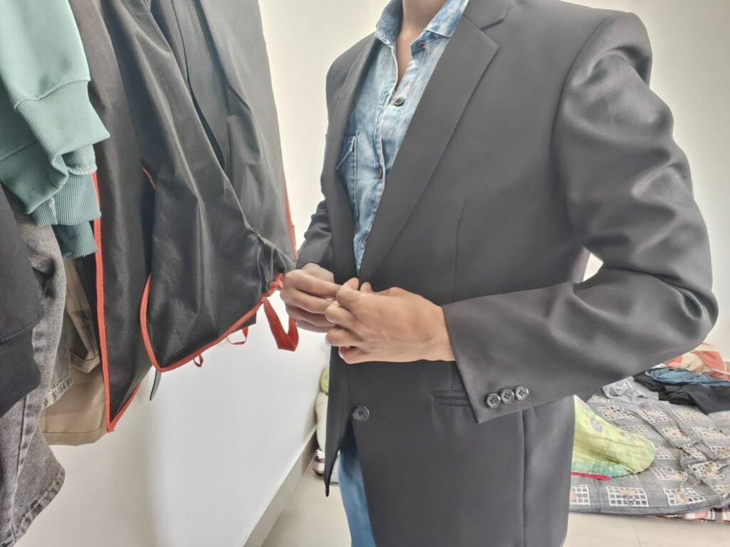 A person is standing in front of a clothing rack, adjusting the buttons on a black blazer. They are wearing...