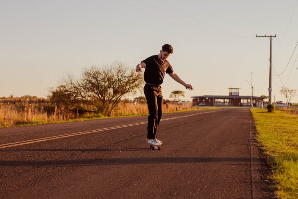 Young man balancing on a skateboard in the middle of an empty road at sunset